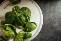Fresh spinach leaves on white plate on grey surface — Stock Photo