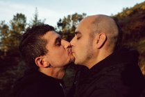 Homosexual couple kissing on path in forest in sunny day — Stock Photo