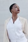 Sinnliche Mode kurzhaariges ethnisches Model im weißen Outfit posiert gegen graue Wand — Stockfoto
