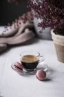 Tasse frisch gebrühten Espresso in Glasschale serviert mit rosa Makronen auf dem Tisch — Stockfoto