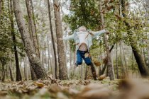 Положительный ребенок прыгает на сухую листву в лесу — стоковое фото