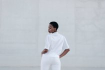 Elegante, kurzhaarige Frau im weißen Outfit posiert gegen graue Bauweise — Stockfoto