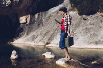 Donna in piedi su roccia con caso vicino acqua limpida nel lago — Foto stock