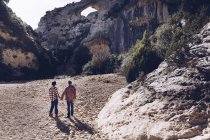 Junges Paar Händchen haltend in Schlucht zwischen Felsbergen bei sonnigem Tag — Stockfoto