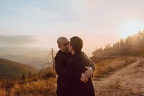 Feliz pareja homosexual abrazándose y besándose en el camino en el bosque en un día soleado - foto de stock