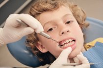 Mãos de dentista em luvas usando ferramentas profissionais para examinar os dentes do menino bonito na clínica — Fotografia de Stock