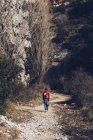 Donna con zaino e custodia camminare su strada rocciosa in maestose scogliere selvagge — Foto stock
