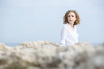 Junge nachdenkliche Frau sitzt an der Küste und blickt in die Kamera — Stockfoto