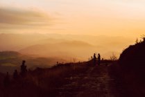Distant homosexual couple embracing near dog on route in mountains at sunset — Stock Photo