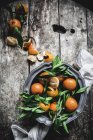 Mandarinas frescas con hojas y plato sobre mesa de madera gris - foto de stock