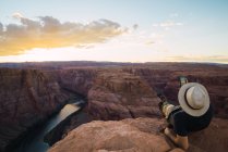 Вид сзади парня, лежащего на скале с мобильным телефоном в красивом каньоне и спокойной реке в солнечный день на Западном побережье США — стоковое фото
