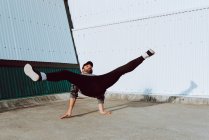 Ragazzo in abito elegante esecuzione flip vicino al muro di edificio moderno sulla strada della città — Foto stock