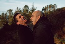 Laughing homosexual couple hugging on path in forest in sunny day — Stock Photo