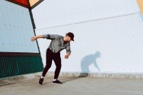 Guy in stylish outfit dancing near wall of modern building on city street — Stock Photo