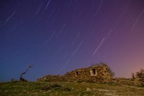 Larga exposición de cielo increíble con estrellas en la noche y construcción de roca envejecida en la colina - foto de stock