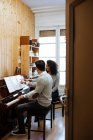 Молодой человек учится играть на фортепиано рядом с черной женщиной, преподавая в музыкальной студии — стоковое фото
