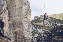 Знизу невизначений альпініст, що висить на мотузці на грубому скелі на блакитному небі — стокове фото