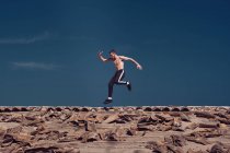 Homem pulando enquanto breakdancing no telhado contra o céu azul — Fotografia de Stock