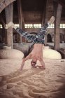 Shirtless young male performing modern dance movement on sandy ground inside aged building — Stock Photo