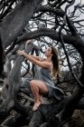 Junge Ballerina in grauer Kleidung posiert auf Ästen trockener Bäume — Stockfoto