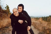 Feliz pareja homosexual divirtiéndose en ruta entre plantas en las montañas - foto de stock