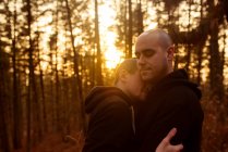 Romantic homosexual couple with closed eyes embracing in forest in evening — Stock Photo