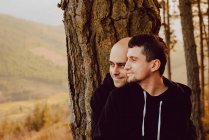 Verträumtes homosexuelles Paar umarmt nahe Baum im Wald und malerischen Blick auf das Tal — Stockfoto
