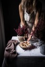Mulher de colheita cozinheiro em avental de corte de bolo de ameixa na mesa com flores — Fotografia de Stock
