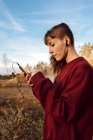 Giovane hipster donna con piercing e auricolari ascoltare musica con telefono cellulare e camminare sulla strada di campagna — Foto stock