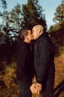 Feliz casal homossexual abraçando e beijando na rota na floresta em dia ensolarado — Fotografia de Stock