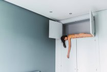 Young sensual woman sleeping on high shelf of wardrobe in bedroom — Stock Photo