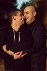 Cheerful homosexual couple embracing in forest in sunny day on blurred background — Stock Photo