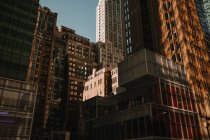 Desde abajo del exterior de los edificios en la densidad en la calle de la ciudad de Nueva York a la luz del sol - foto de stock