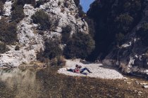 Vue latérale du jeune couple couché sur la côte rocheuse de la rivière de montagne près de la falaise — Photo de stock
