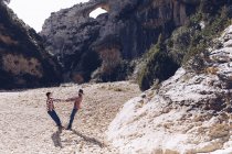 Молода пара тримає руки в каньйоні між скелястими горами в сонячний день — стокове фото