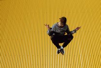 Schöner bärtiger Kerl im schicken Outfit springt gegen gelbe Wand eines modernen Gebäudes — Stockfoto