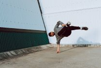 Cara realizando suporte de mão enquanto dança perto da parede do edifício moderno na rua da cidade — Fotografia de Stock