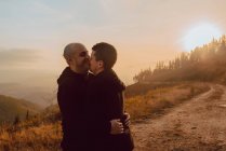 Feliz casal homossexual abraçando e beijando no caminho na floresta em dia ensolarado — Fotografia de Stock
