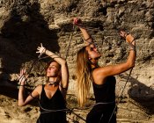 Young mysterious women in black wear with closed eyes tangling in twist near rocks in sunny day — Stock Photo