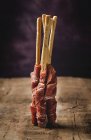 Gressinis avec jambon serrano typique espagnol sur table en bois sur fond sombre — Photo de stock