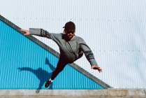 Ragazzo in abito elegante esecuzione flip vicino al muro di edificio moderno sulla strada della città — Foto stock