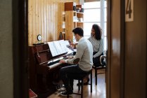 Jeune homme apprenant à jouer du piano près de la femme noire enseignant dans un studio de musique — Photo de stock