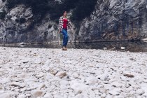 Lässige Frau trägt Koffer und geht am Ufer des klaren Wasserflusses in der Natur spazieren — Stockfoto