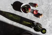 Fraises fraîches dans un bol et sur une surface grise avec bouteille de vin — Photo de stock