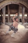 Молодой человек без рубашки танцует на песке в помещении — стоковое фото