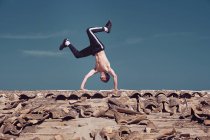 Man doing handstand on roof against blue sky — Stock Photo