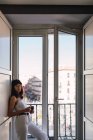 Junge schlanke Frau mit Mütze blickt in die Kamera und steht in der Nähe des Balkons — Stockfoto