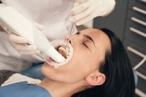 Mãos de dentista em luvas e máscara usando equipamento moderno para fazer a varredura de dentes de paciente feminino em consultório odontológico — Fotografia de Stock