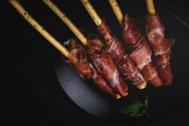 Gressini con tipico prosciutto serrano spagnolo su piatto su fondo nero — Foto stock