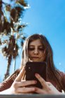 Девочка-подросток смотрит на свой смартфон на улице в солнечный день — стоковое фото